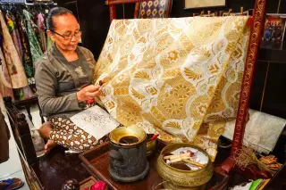 Ilustrasi: Seorang wanita sedang membatik kain tradisional menggunakan canting dan wajan malam kecil.