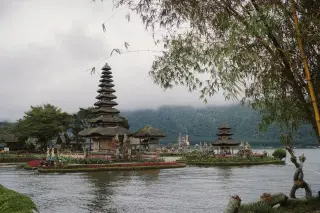 Ilustrasi: Pemandangan Pura Ulun Danu Beratan di tepi danau dengan latar belakang perbukitan berkabut.