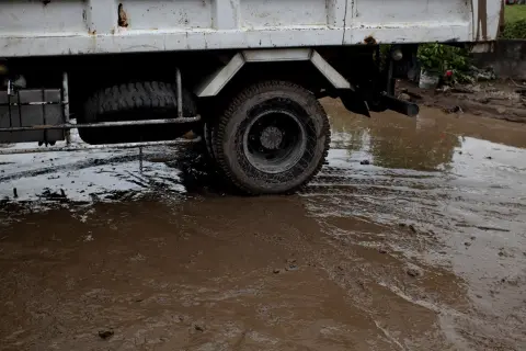 Ilustrasi: Sebagian badan truk putih melintasi genangan air dan jalanan berlumpur tebal.