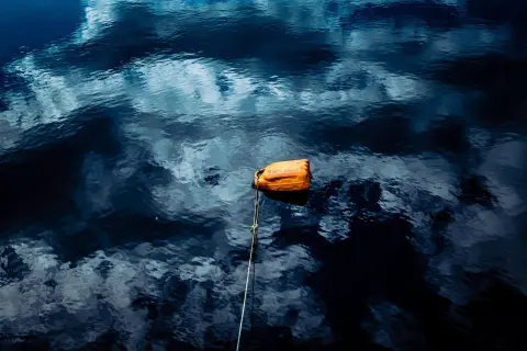 Ilustrasi: Sebuah jeriken oranye terapung di permukaan air laut yang memantulkan langit.