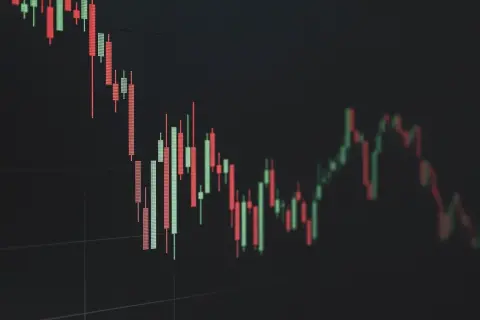 Ilustrasi: Tampilan grafik candlestick saham merah dan hijau pada layar berlatar belakang gelap.