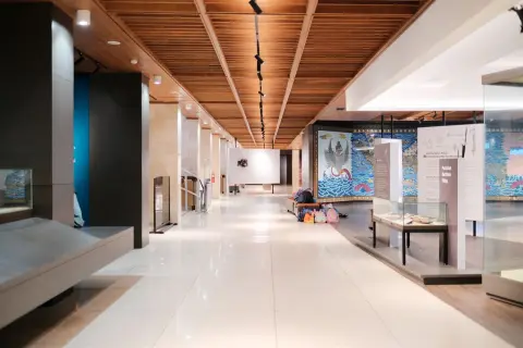 Ilustrasi: Lorong galeri museum modern yang luas dengan etalase kaca dan panel informasi.