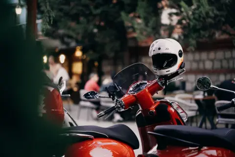 Ilustrasi: Helm putih terpasang pada stang skuter merah yang sedang parkir di luar ruangan.
