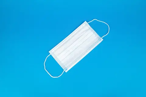 Ilustrasi: Sebuah masker medis putih diletakkan di atas latar belakang biru cerah.