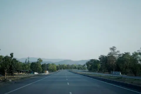 Ilustrasi: Pemandangan jalan raya beraspal yang lurus dan sepi dengan pepohonan di tepinya.