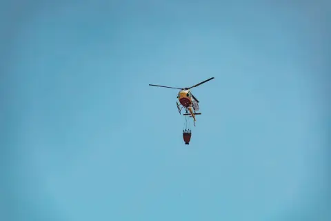 Ilustrasi: Sebuah helikopter pemadam membawa kantong air terbang di bawah langit biru.