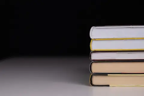 Ilustrasi: Tumpukan buku bersampul tebal di atas meja dengan latar belakang gelap.