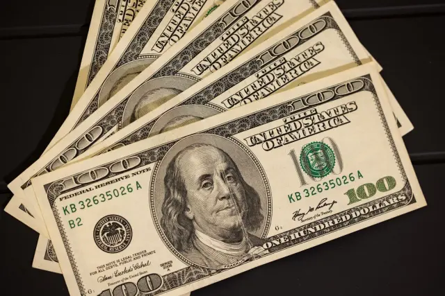 Ilustrasi: Beberapa lembar uang kertas seratus dolar AS tersusun di atas permukaan gelap.