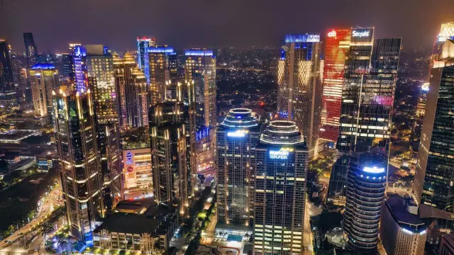 Ilustrasi: Pemandangan malam deretan gedung pencakar langit berlampu dan jalan raya perkotaan dari atas.