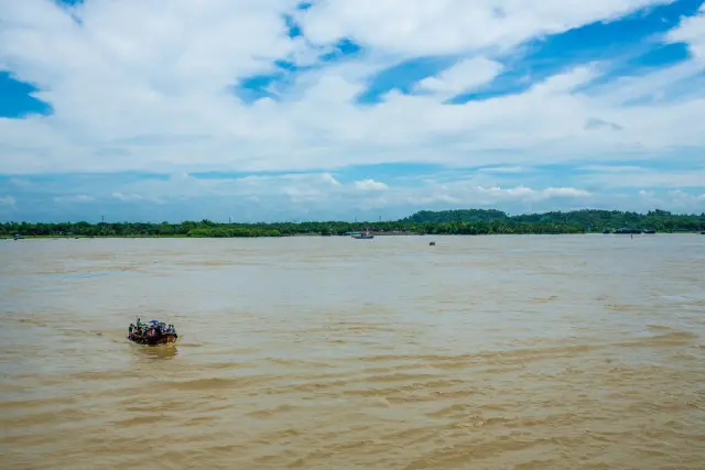 Ilustrasi: Sebuah perahu kecil sarat penumpang melintasi sungai yang sangat lebar di bawah langit berawan.